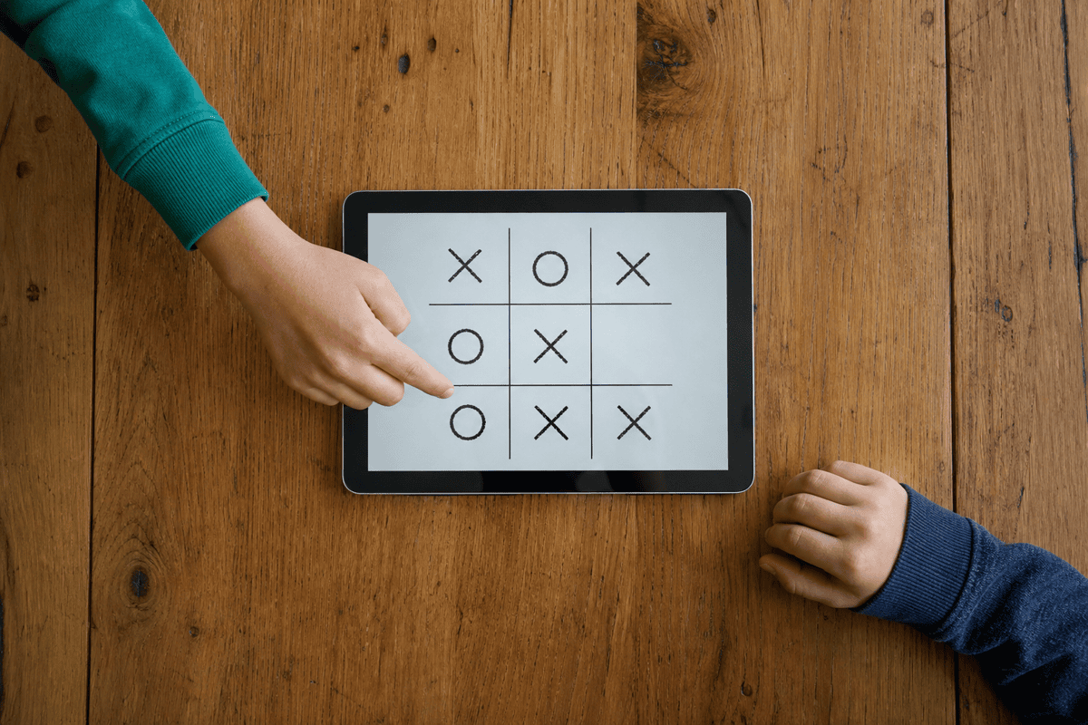 Twee kinderen spelen boter kaas en eieren samen op één tablet op tafel