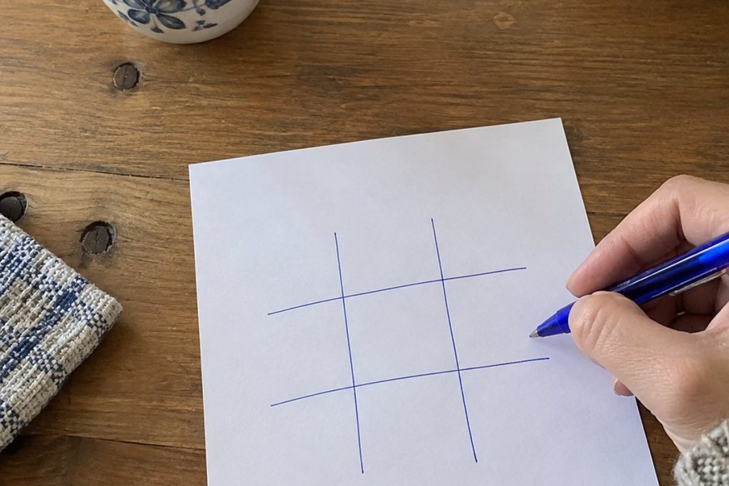 Een hand tekent een leeg boter kaas en eieren raster met een blauwe pen op papier